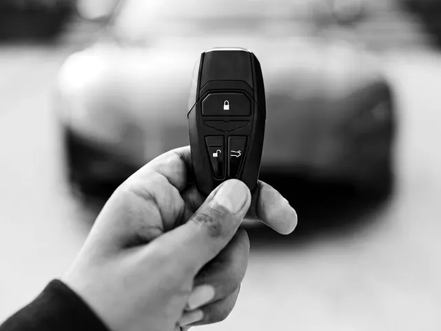 Hand holding a car key fob in front of a parked car