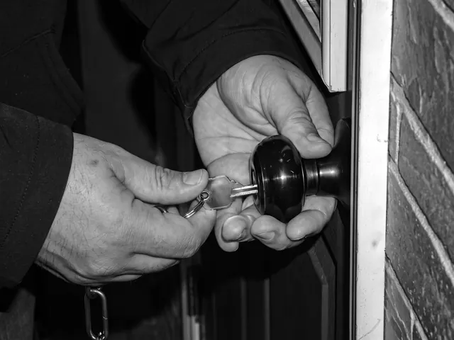 Hands turning a key in a black door knob on a brick house