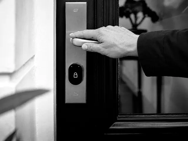 Hand on a lever handle of a dark entry door with a smart lock unit below it
